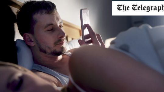 Man looking at his phone while in bed with his partner