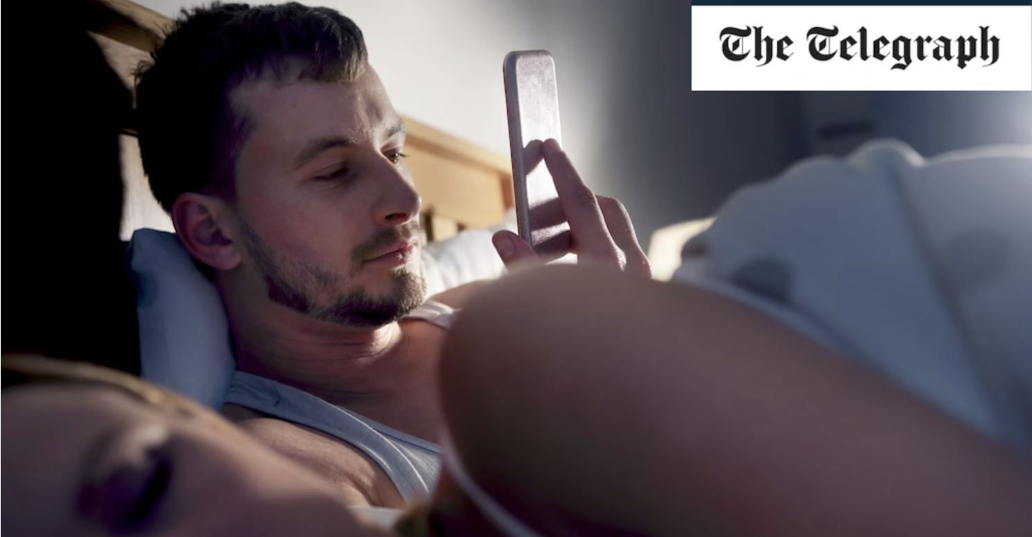 Man looking at his phone while in bed with his partner